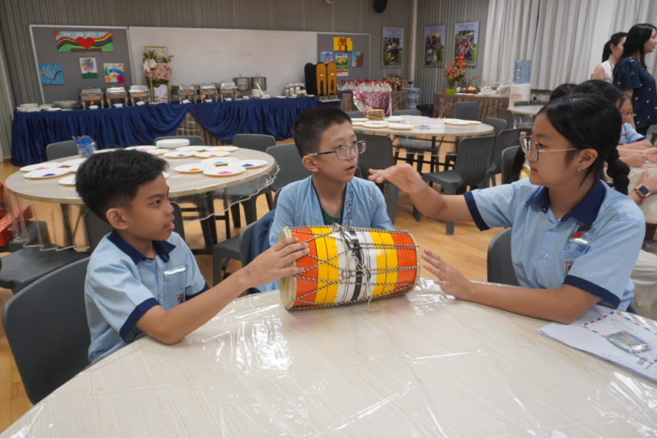 Two boys and a girl at a table playing a colorful drum.